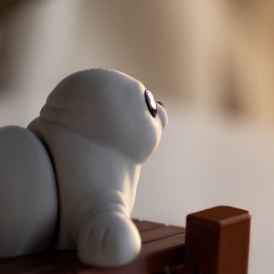 May include: A gray baby seal figurine with black eyes, sitting on a wooden surface. The figurine is made of a soft, pliable material and has a realistic appearance.  Baby Seal.