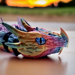 May include: A colourful dragon head figurine with a blue eye, made using a 3D printer. The dragon head is made of a rainbow of colours, including pink, yellow, blue, and green.