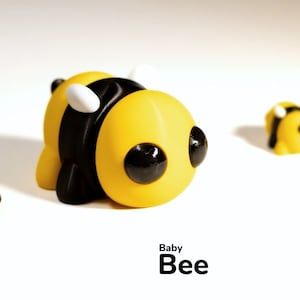 May include: Five yellow and black bee figurines with white wings and black eyes. The largest bee is lying on its side. The text "Baby Bee" is printed below the figurines.