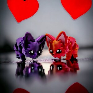 Puede incluir: Dos peque&ntilde;as figuritas de animales de estilo de dibujos animados. Una es morada y la otra es naranja. Ambas se miran.
