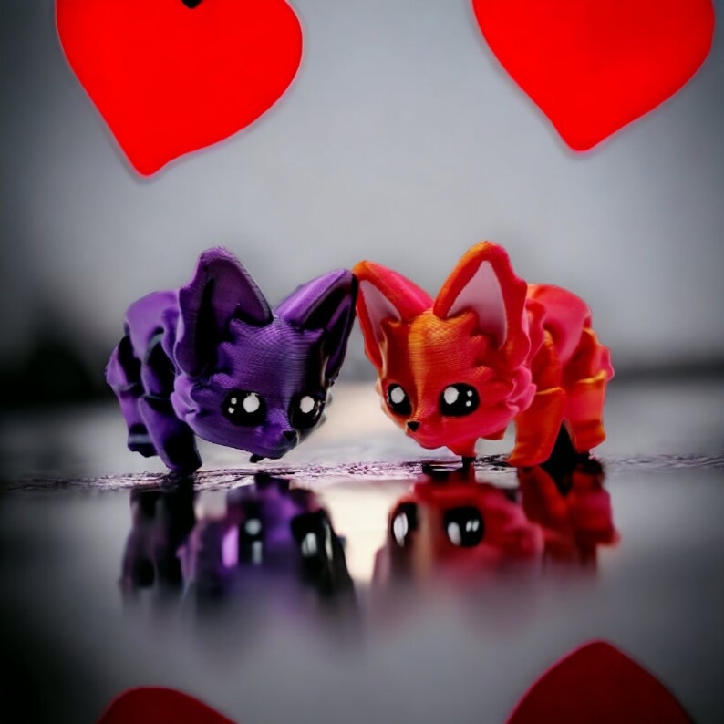 Puede incluir: Dos peque&ntilde;as figuritas de animales de estilo de dibujos animados. Una es morada y la otra es naranja. Ambas se miran.