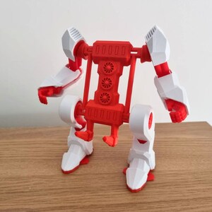 May include: A red and white articulated robot toy with wheels. The robot has a large red body with four white wheels and a red frame. The robot's arms and legs are articulated and can be moved into different positions.
