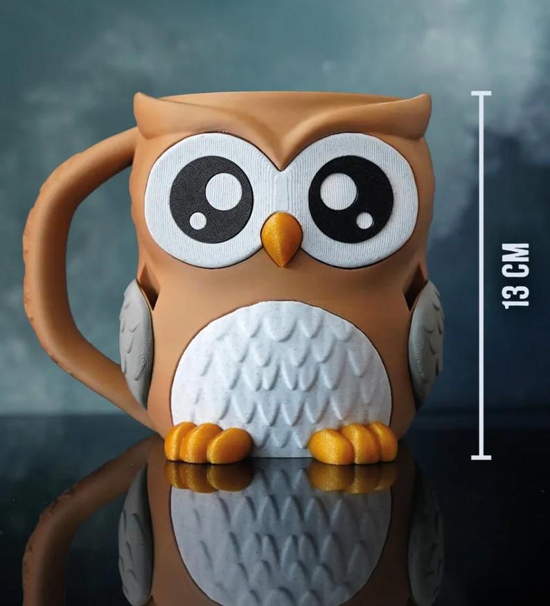 May include: A brown owl-shaped mug with large white eyes and a yellow beak. The mug has a handle and is 13 cm tall. The owl's chest is white with a textured pattern, and it has orange feet.