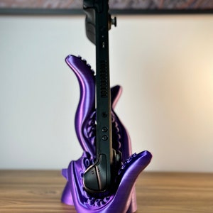 May include: A purple 3D printed stand shaped like a monster's mouth holding a black Nintendo Switch.
