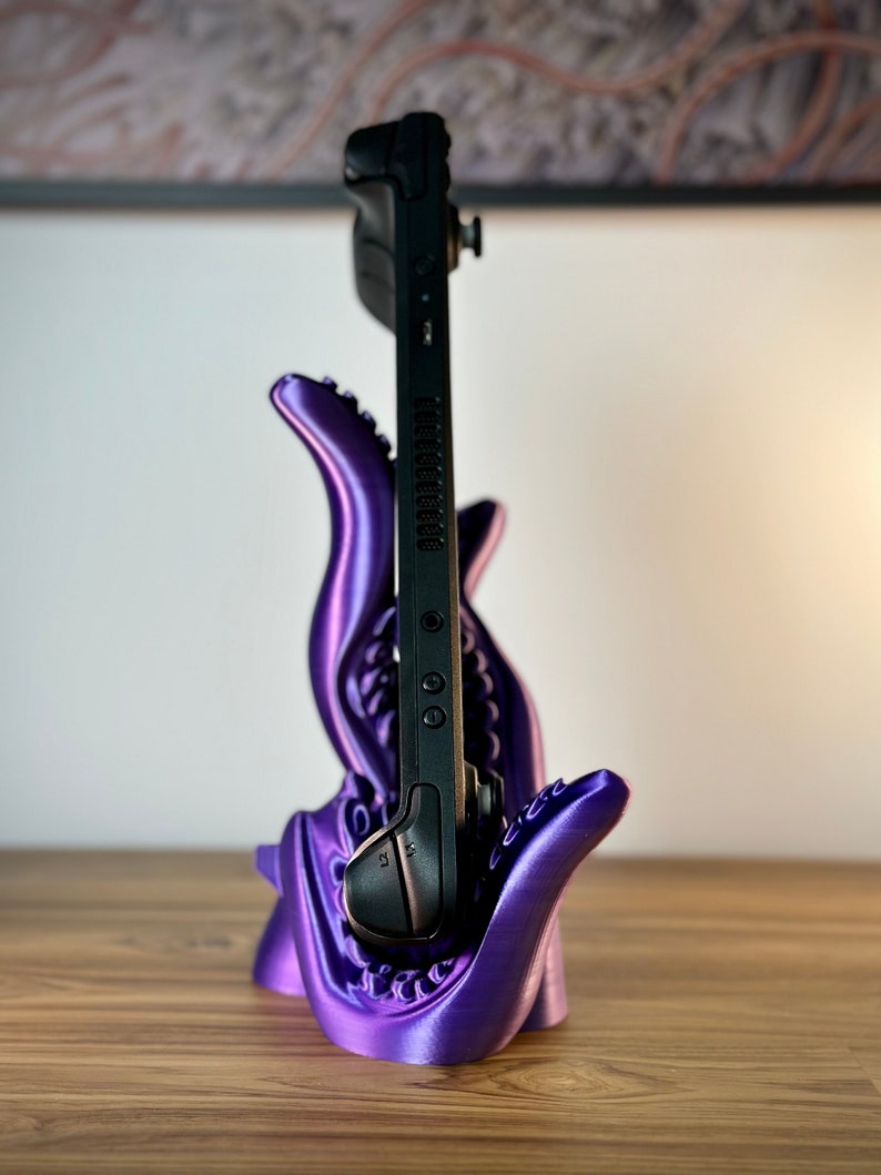 May include: A purple 3D printed stand shaped like a monster's mouth holding a black Nintendo Switch.