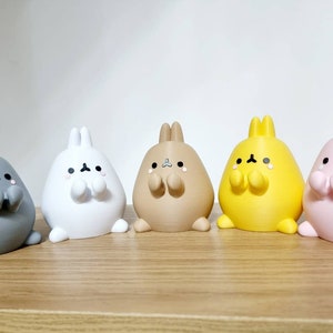 K&ouml;nnte beinhalten: F&uuml;nf kleine Pl&uuml;sch-Hasenfiguren in verschiedenen Farben: Grau, Wei&szlig;, Braun, Gelb und Rosa. Jeder Hase hat einen runden K&ouml;rper, kurze Beine und einen s&uuml;&szlig;en Ausdruck mit geschlossenen Augen und kleinen, erhobenen Armen.