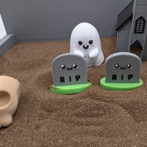 Pu&ograve; includere: Una scena di cimitero di Halloween con un fantasma bianco, due lapidi grigie con la scritta "RIP" su di esse e un teschio marrone. Le lapidi hanno dei volti carini disegnati su di esse.