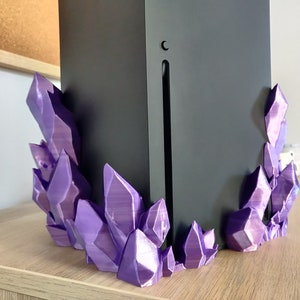 Puede incluir: Un soporte de cristal morado impreso en 3D para una consola de juegos. El soporte est&aacute; hecho de m&uacute;ltiples formas de cristal que est&aacute;n dispuestas de una manera que se asemeja a un c&uacute;mulo de cristales.