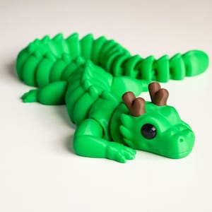 May include: A green dragon figurine with brown antlers. The dragon has a segmented body and large, black eyes.