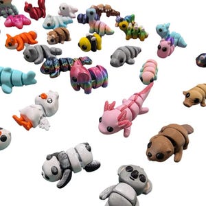 Peut inclure: Une collection de figurines d'animaux miniatures color&eacute;es, dont un panda, un koala, un axolotl et un canard. Les figurines sont faites d'un mat&eacute;riau lisse et pr&eacute;sentent diverses couleurs et motifs. Les animaux sont dispers&eacute;s sur un fond blanc.