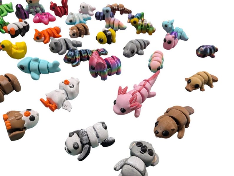Peut inclure: Une collection de figurines d'animaux miniatures color&eacute;es, dont un panda, un koala, un axolotl et un canard. Les figurines sont faites d'un mat&eacute;riau lisse et pr&eacute;sentent diverses couleurs et motifs. Les animaux sont dispers&eacute;s sur un fond blanc.
