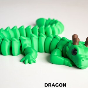 May include: A green 3D printed dragon figurine with brown antlers. The dragon is curled up in a sleeping position with its head resting on its front paws.