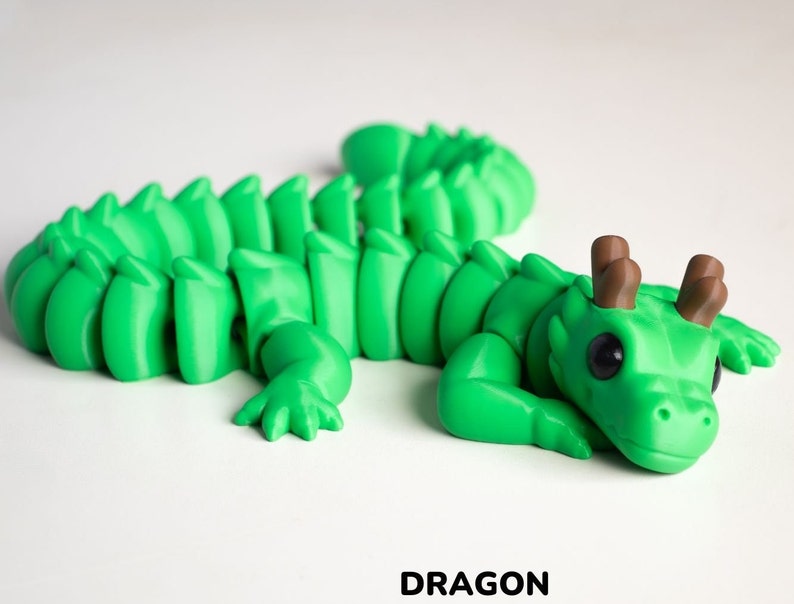 May include: A green 3D printed dragon figurine with brown antlers. The dragon is curled up in a sleeping position with its head resting on its front paws.