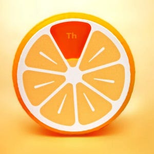 May include: A round, orange-colored object resembling a citrus fruit slice, with white segments and a bright orange rind. The top segment is a darker orange and has the letters "Th" printed on it.