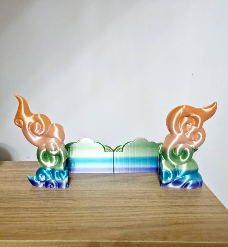 May include: A 3D printed decorative object with a rainbow gradient design. The object is shaped like a cloud with a swirling pattern. It is made of plastic and has a smooth finish.