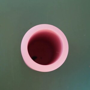 May include: A top-down view of a light pink, circular object with a hollow center. The inside of the object is a darker shade of pink. The object is set against a muted green background.