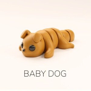 May include: A brown, cartoon-style baby dog toy with large black eyes. The toy is made of a soft, pliable material and is shaped like a curled-up puppy. The text "BABY DOG" is printed below the toy.