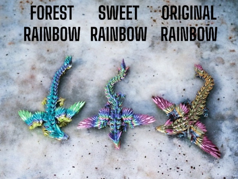 May include: Three origami dragons made of iridescent paper. The dragons are in different color schemes: forest rainbow, sweet rainbow, and original rainbow. The dragons are all facing the same direction with their wings spread out.