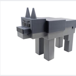 May include: A grey, blocky dog sculpture with a geometric design. The dog has a rectangular body, square legs, and a head with pointed ears. The sculpture is made of a solid material and stands on a white background.