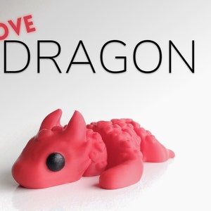 May include: A small, red, 3D printed dragon figurine with black eyes. The dragon is lying on its belly with its head turned to the side. The text "LOVE DRAGON" is written in black letters above the dragon.