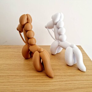 May include: Two balloon animal sculptures, one brown and one white, in the shape of a horse. The sculptures are made of a smooth, rubber-like material and have a realistic appearance.