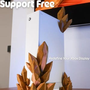 May include: A white Xbox Series X console with brown crystal-shaped decorative accents. The text "Support Free" and "Redefine Your Xbox Display" are visible. The crystals are placed around the console.