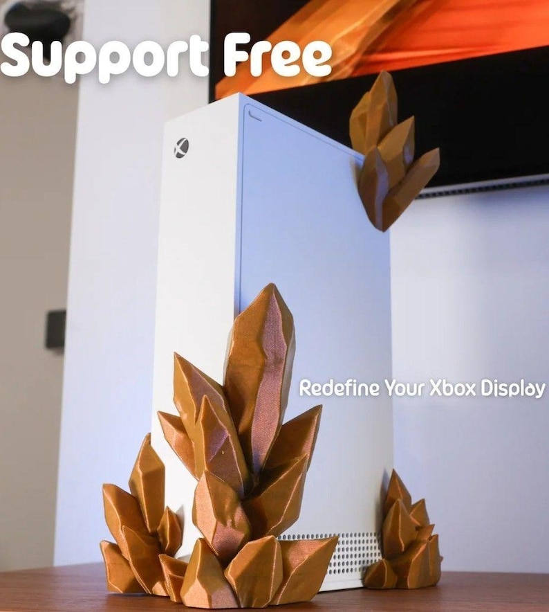 May include: A white Xbox Series X console with brown crystal-shaped decorative accents. The text "Support Free" and "Redefine Your Xbox Display" are visible. The crystals are placed around the console.