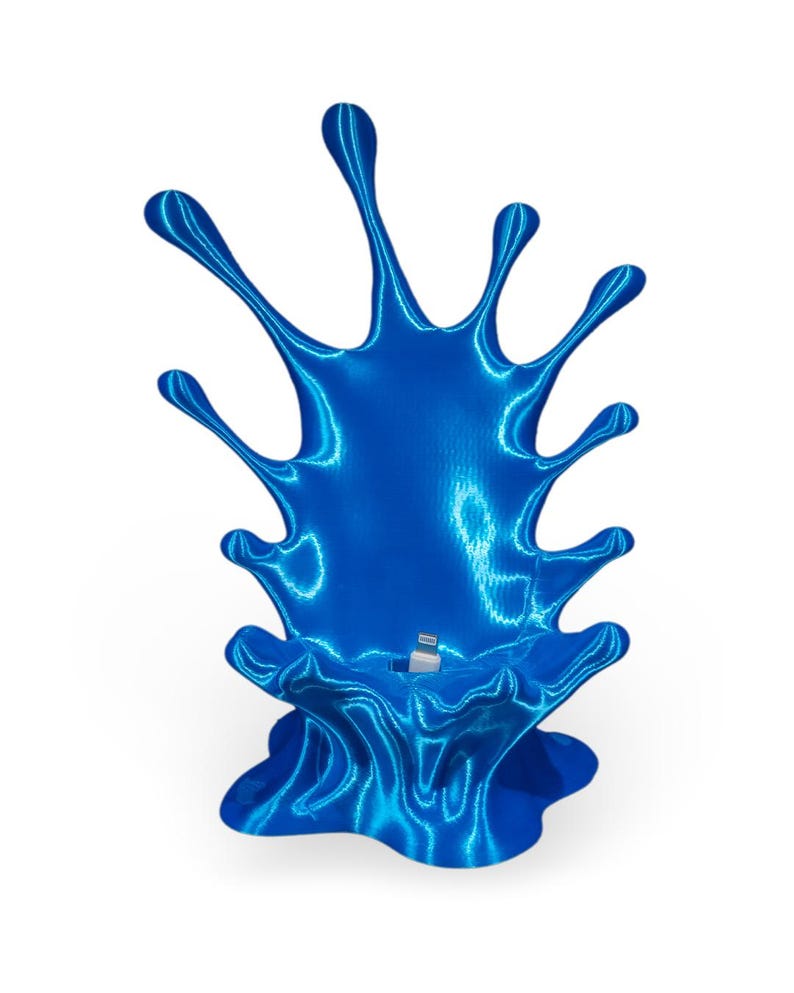 May include: A blue 3D printed phone stand shaped like a splash of liquid. The stand has a small opening for a charging cable.