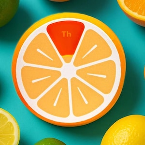 May include: A round, orange-colored coaster with a citrus fruit design. The coaster has a white outline and a segment colored red with the letters "Th". Other citrus fruits, including oranges, lemons, and limes, are scattered around the coaster on a teal background.