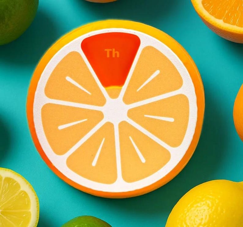 May include: A round, orange-colored coaster with a citrus fruit design. The coaster has a white outline and a segment colored red with the letters "Th". Other citrus fruits, including oranges, lemons, and limes, are scattered around the coaster on a teal background.