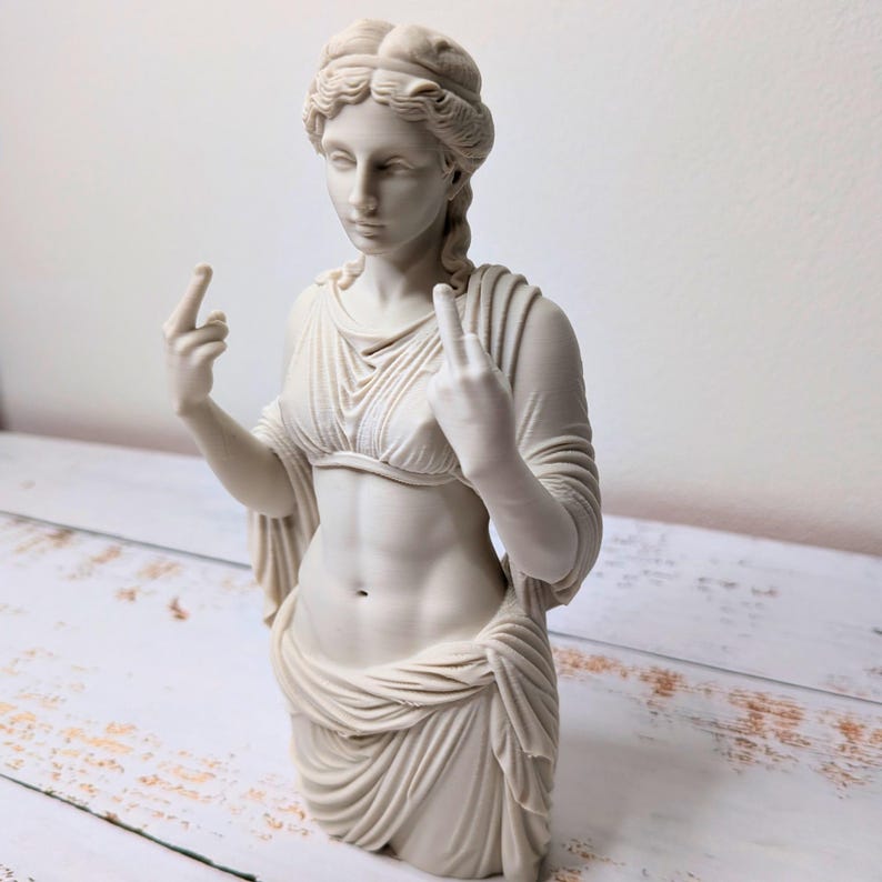 May include: A cream-colored bust sculpture of a classical figure with wavy hair, wearing a draped garment that leaves the midriff exposed. The figure is depicted with both hands raised, extending the middle finger on each hand in a gesture.