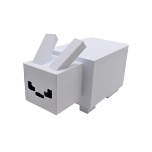 May include: A white, geometric rabbit sculpture with upright ears and black facial details. The rabbit is made from blocky shapes, giving it a pixelated look. The design is reminiscent of a video game character.