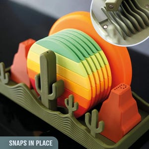 May include: A colorful dish rack with a desert theme. The rack features a green base with cactus and mountain shapes. The plates are stacked in rainbow colors. The text "SNAPS IN PLACE MAGNETICALLY" is visible.