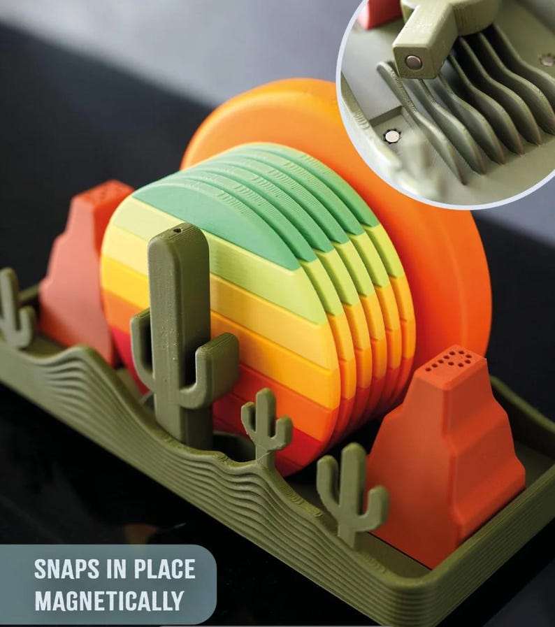 May include: A colorful dish rack with a desert theme. The rack features a green base with cactus and mountain shapes. The plates are stacked in rainbow colors. The text "SNAPS IN PLACE MAGNETICALLY" is visible.