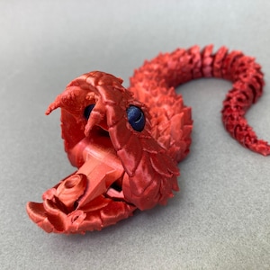 May include: A red 3D printed model of a snake with its mouth open, revealing a detailed interior. The snake has a textured, scaly body and blue eyes.