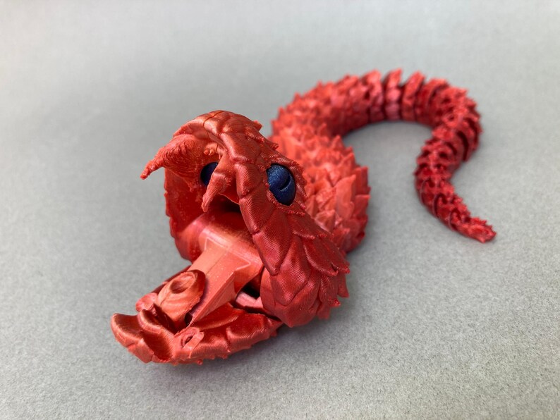 May include: A red 3D printed model of a snake with its mouth open, revealing a detailed interior. The snake has a textured, scaly body and blue eyes.