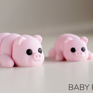Puede incluir: Dos peque&ntilde;as figuras de cerdos rosas con ojos negros y caras sonrientes. Un cerdo est&aacute; segmentado, el otro es de una sola pieza. El texto "BABY PIG" est&aacute; debajo.