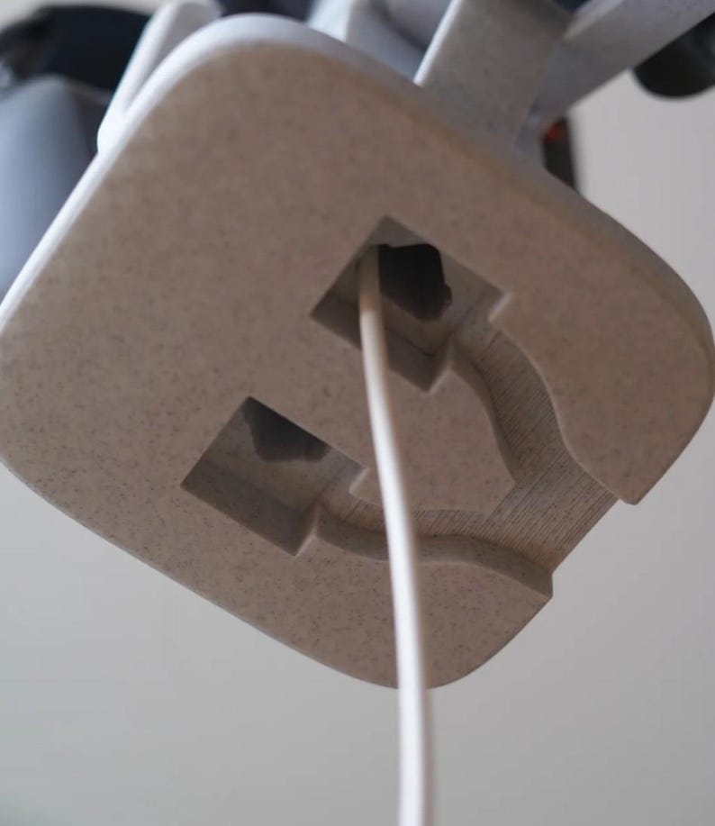 May include: Close-up of a light beige, textured, square-shaped object with a rectangular cutout and a white cord extending from it. The object appears to be part of a larger structure, possibly a lamp or electronic device.