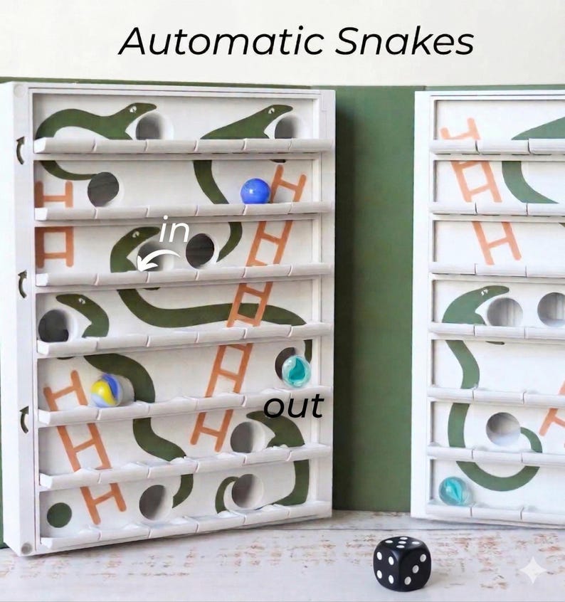 May include: A white wooden game with green snake illustrations, orange ladders, and the text "Automatic Snakes." The game includes colorful marbles and a black and white die. The word "in" and "out" are also visible.