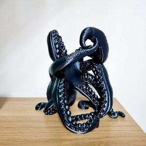 May include: A black octopus sculpture with detailed tentacles, made with a 3D printer. The octopus is curled up in a compact shape, with its tentacles intertwined.