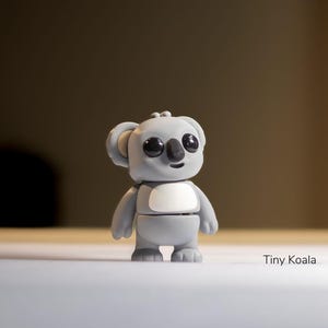 May include: A gray koala figurine with black eyes and a white belly. The figurine is standing on a white surface. The text "Tiny Koala" is written below the figurine.