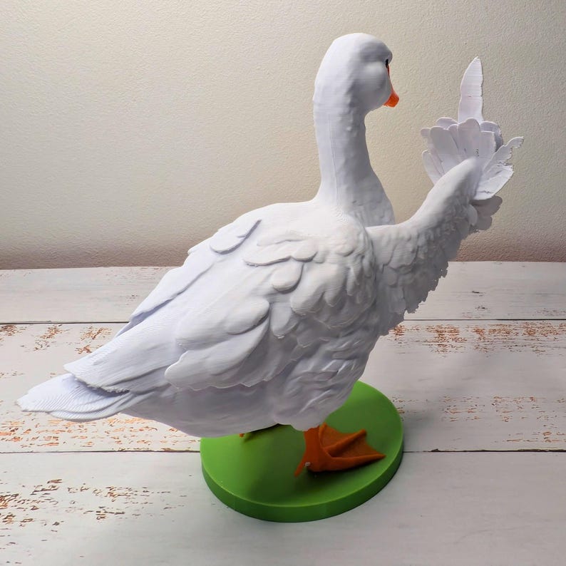 May include: A white goose ornament with outstretched wings, an orange beak and feet, and a green base. The goose has detailed feather textures. The ornament is a decorative item.
