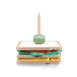 May include: A wooden sandwich toy with layers of bread, tomato, lettuce, and cheese. A wooden toothpick with a green base is inserted into the sandwich. The toy is designed to resemble a sandwich.