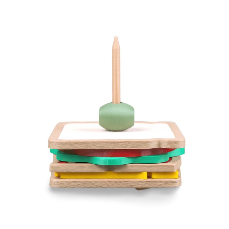 May include: A wooden sandwich toy with layers of bread, tomato, lettuce, and cheese. A wooden toothpick with a green base is inserted into the sandwich. The toy is designed to resemble a sandwich.