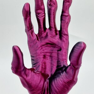 May include: A 3D printed hand sculpture with a metallic silver base. The hand is made of a deep pink, almost magenta, plastic and is posed with the palm facing forward.
