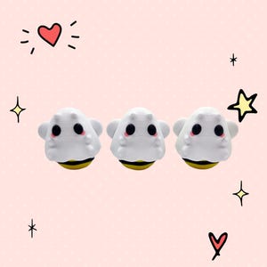 May include: Three white and yellow bee-themed eraser toppers with black eyes and pink cheeks. The erasers are on a pink background with white polka dots and hearts.