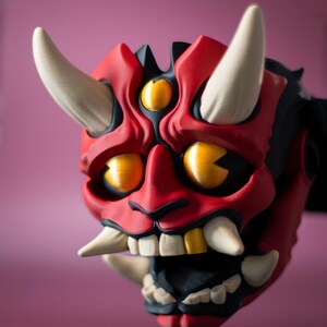 May include: A red and black Oni mask with three eyes and large white horns. The mask has a wide open mouth with white and gold teeth. The background is a solid pink color.