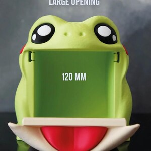 May include: A lime green frog-shaped container with a large opening. The frog has large black and white eyes, red accents, and a red mouth. The opening measures 120 mm. The text "LARGE OPENING" is above the opening.