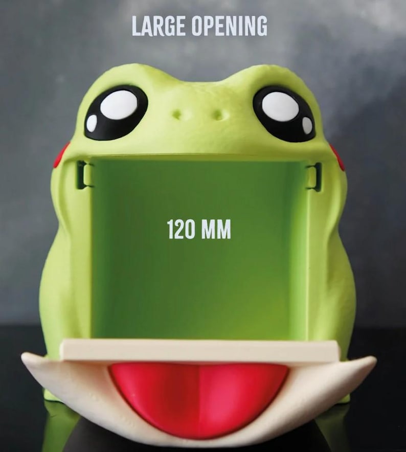 May include: A lime green frog-shaped container with a large opening. The frog has large black and white eyes, red accents, and a red mouth. The opening measures 120 mm. The text "LARGE OPENING" is above the opening.