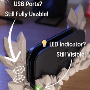 May include: A black Nintendo Switch console sits in a white, rock-like stand. The stand has two USB ports and an LED indicator. Text on the image reads "USB Ports? Still Fully Usable!" and "LED Indicator? Still Visible!"